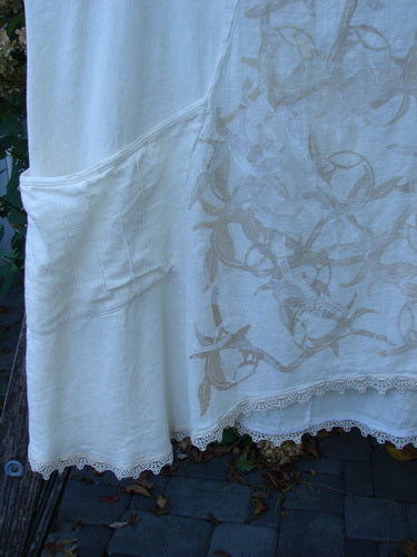 Barclay Slub Figure 8 Lace Pocket Pinafore Dress in Soft Floral Crème Size 2, featuring a subtle vine print, lace hem, roomy side pocket, and distinctive figure-eight seams, hangs outdoors.