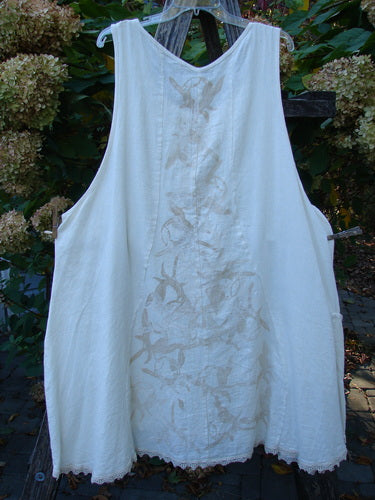 Barclay Slub Figure 8 Lace Pocket Pinafore Dress in Soft Floral Crème, featuring an A-line shape with vine embroidery, scalloped hem, and unique figure-eight seams, hanging outdoors.