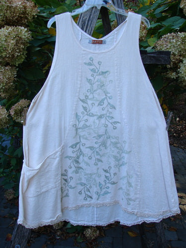 Barclay Slub Figure 8 Lace Pocket Pinafore Dress in Soft Floral Crème, featuring scoop neckline, side pockets, delicate green botanical print, crochet hem, and distinctive figure-eight seams, hanging outdoors on a plastic hanger.