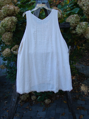 Barclay Slub Figure 8 Lace Pocket Pinafore Dress Soft Floral Crème Size 1 features a loose A-line shape, delicate lace hem, unique figure-eight seams, and exterior pockets, displayed on a wooden hanger outdoors.