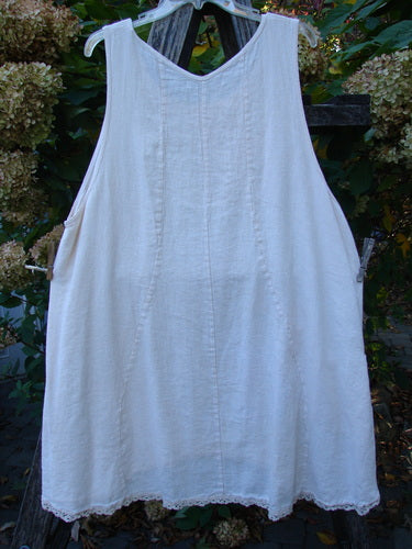 Barclay Slub Figure 8 Lace Pocket Pinafore Dress Soft Floral Crème Size 1, featuring unique figure-eight seams, lace hem, and exterior pockets, elegantly displayed outdoors against a backdrop of foliage and blooms.