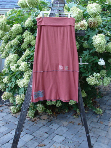 Barclay Patched Thermal Fold Over Ruffle Panel Skirt, Size 2: A dress on a rack with a pink dress featuring blue stitching, a skirt on a wooden ladder, and a close-up of a flower and plant.