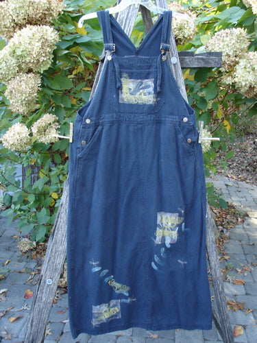 1996 Denim Overall Jumper Truck Travel Black Size 1: Dark-blue denim jumper dress with adjustable straps, metal buckles, bib pocket, side pockets, and colorful fabric patches, hanging on a wooden ladder outdoors.