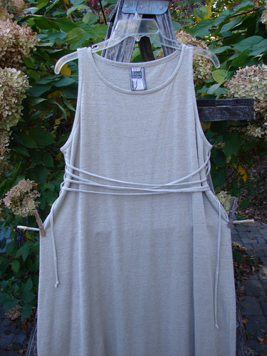 1998 Linen Knit Wrap Dress Unpainted Natural Size 1 drapes elegantly on a wooden trellis, showcasing its ankle-length design, slender silhouette, and waist-cinching cord, embodying timeless BlueFishFinder vintage style.