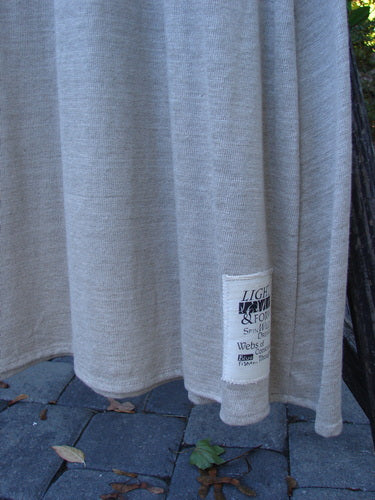 1998 Linen Knit Wrap Dress Unpainted Natural Size 1, elegantly draped outdoors, showcasing its flowing linen knit texture and signature patch near the hem against a backdrop of paving stones and a tree trunk.