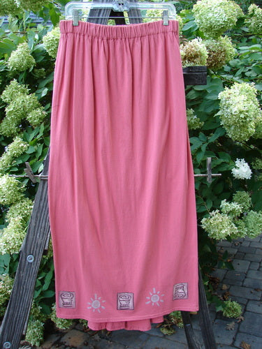 Image alt text: "1995 Kick Pleat Skirt in Papaya, featuring a pink skirt on a wooden ladder, a clothesline, a plant, a wood plank, a white flower, and a bush"