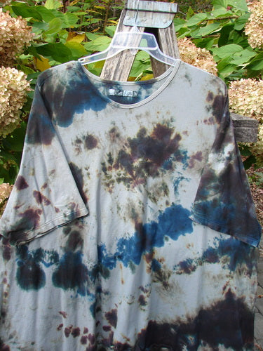 Barclay Drawcord Art Top Mottled Night Storm OSFA hangs on a clear plastic hanger, showcasing its A-line shape, wide sleeves, and nifty drawcord back against a rustic garden chair backdrop.