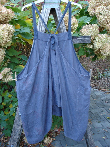 Barclay Linen Apron Jumper Celtic Rain Raven Size 2 displayed on a wooden garden ladder, featuring a sleeveless design, bib front, unique striped adjustable straps, and large side patch pockets.