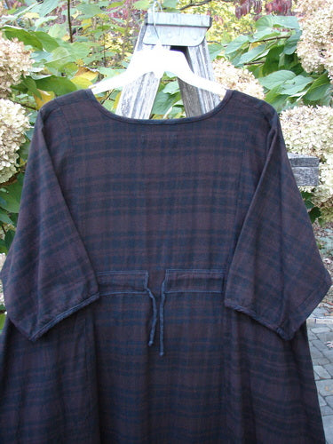 Barclay Flannel Keyhole Drawcord Pocket Dress Brum Plaid Size 2 features a loose fit, ¾-length sleeves, wide scooped neckline, and drawstring waist, hanging outdoors with garden foliage backdrop.