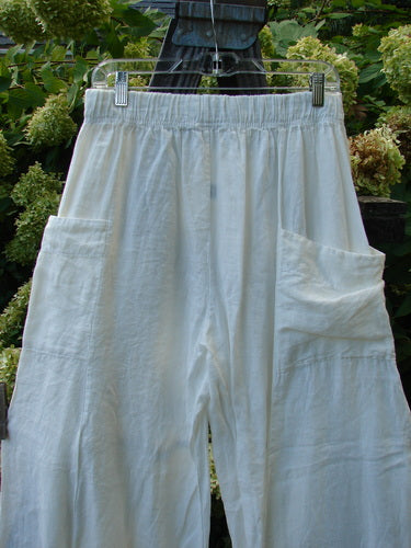 A pair of Barclay Linen Side Pocket Pepper Pants in white, size 1. These pants are made from medium weight linen and feature a full elastic waistline, a billowy shape, and a slightly cropped length. They have two exterior front side back wrap pockets and sectional panels. The pants come unpainted, allowing for easy mixing and matching with other pieces. Waistline relaxed: 30, waistline fully extended: 40, hips: 66, inseam: 28, length: 42 inches.