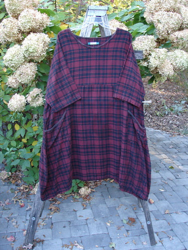 Barclay Flannel Bottom Bell Pocket Dress in Merlo Plaid Size 2, featuring a graceful drape over a rustic ladder, showcasing its rounded neckline, curved empire waist, and varying hemline.