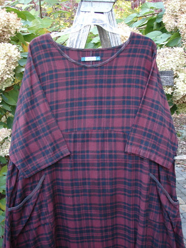 Barclay Flannel Bottom Bell Pocket Dress Merlo Plaid Size 2, featuring a loose-fitting tunic style with wide three-quarter sleeves and slouchy side pockets, displayed hanging on a wooden ladder outdoors.