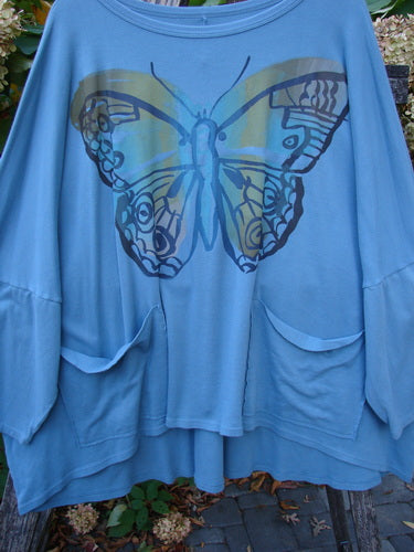 Barclay NWT Two Pocket Mariposa Pullover Butterfly Sea OSFA features a loose-fitting, light blue tunic with a scooped neckline, dolman sleeves, two patch pockets, and a stylized butterfly graphic on the chest.