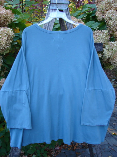 Barclay NWT Two Pocket Mariposa Pullover Butterfly Sea OSFA, a loose-fitting, long-sleeved top with dolman shoulders, wide sleeves, and dual front pockets, hanging on a wooden hanger outdoors.