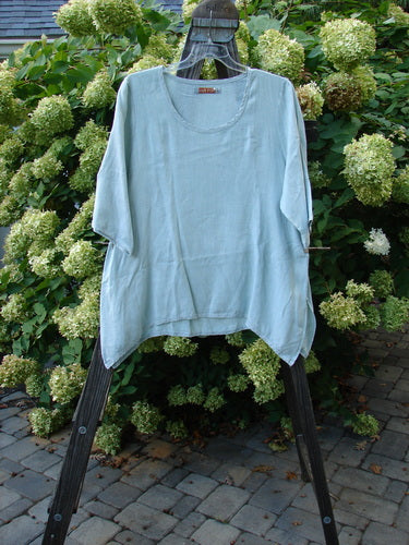Image alt text: Barclay Linen Cross Dye T Top Unpainted Sage Size 1: A blue shirt with a swinging A-line shape, featuring a wooden post in the background.