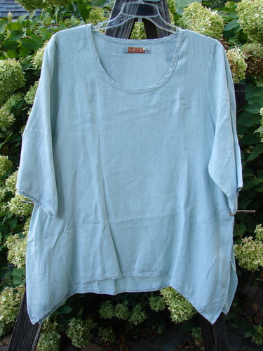 Image: A light blue shirt on a hanger, with a close-up of a person's leg and a glass.

Alt text: Barclay Linen Cross Dye T Top Unpainted Sage Size 1, a swinging A-line shirt made from medium weight linen. Perfect condition.