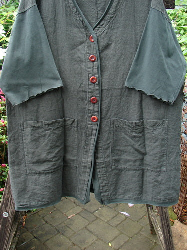 Barclay Cotton Sleeve Pocket Cardigan Unpainted Black Forest Size 1, featuring red wooden buttons, an upward curved hemline, deep V-neck, drop shoulders, curly sleeves, and squared front pockets on a clothes rack.