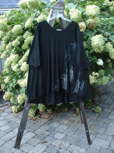 A black Barclay Hi Low Tunic Top on a wooden rack, featuring a soft neckline, varying hemline, and tall neck bottle theme paint. Size 2, made from organic cotton.