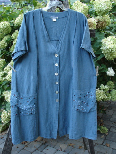 Barclay Linen Double Tie Back Jacket, Rain Shower Dusty Blue Teal. A blue dress with pockets on a clothesline, close-up of a plant.