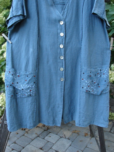 Image: A blue dress with pockets, shown from the front. The dress has a deep V-shaped neckline, a huge A-line sweep, and exterior vertical stitchery. It features front drop flop pockets and a varying hemline. The upper rear shoulder has a drawstring. The dress is made from medium-weight linen and is painted in the suggestive rain shower theme. Size 2. 

Note: The alt text has been modified to fit within the character limit and to align with the provided product description and store context.