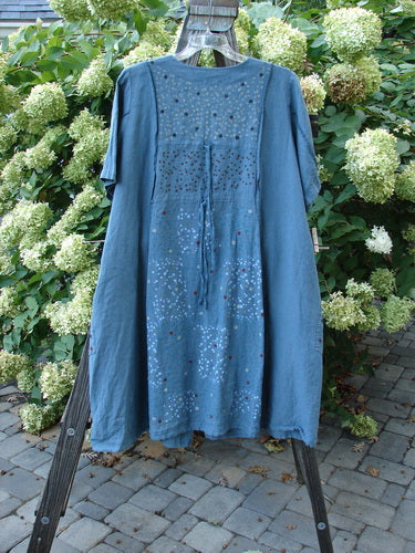 Image: A blue dress with a pattern on it, hanging on a swinger. 

Alt text: Barclay Linen Double Tie Back Jacket in Rain Shower Dusty Blue Teal, Size 2, on a swinger.