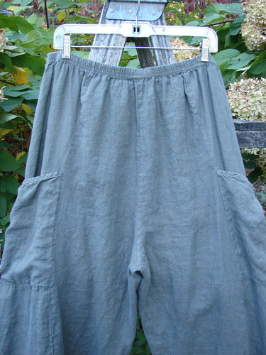 Barclay Lightweight Linen Side Pocket Pant Unpainted Army Stone Size 2 features a gathered elastic waistband, roomy legs, and large side pockets, hanging on a plastic hanger against a leafy backdrop.