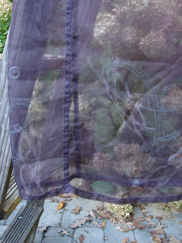 2000 Silk Organza Skirt Wind Whisp Aubergine Size 1 draped over a railing, showcasing its translucent purple fabric and swirling blue-green motif, embodying graceful movement with a Celtic wind theme.