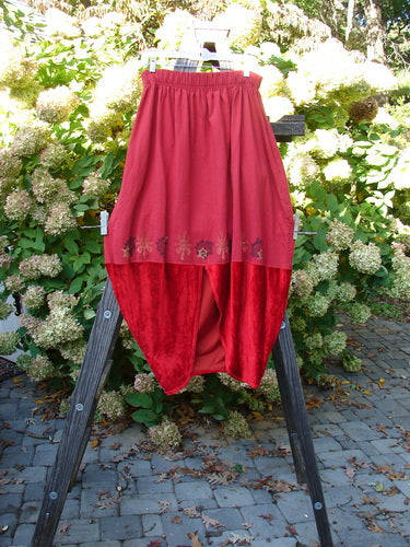 1996 Velvet Sophia Skirt Celtic Abstracts Pomegranate Size 1: A red skirt on a wooden stand, featuring a bell-shaped upper and a painted velvet lower panel. The skirt has a rear kick vent, a super pegged lower shape, and a 2-inch elastic waistline. Waist: 30-40, Hips: 60, Length: 39 inches.