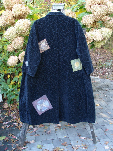 1998 Patched Tapestry Coat Bountiful Sun Guy Black OSFA, featuring a swirling damask pattern, colorful appliqué patches, angular pockets, and vintage buttons, draped elegantly on an outdoor wooden ladder.