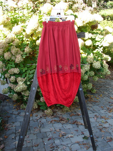 1996 Velvet Sophia Skirt, a red skirt on a wooden stand. Bell-shaped upper with a painted velvet lower panel. Rear kick vent, super pegged lower shape. 2-inch elastic waistline, deeply pocketed. Waist 30-40, hips 60, length 39 inches.
