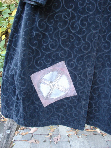1998 Patched Tapestry Coat Bountiful Sun Guy Black OSFA hanging outdoors, showcasing a swirling damask pattern with a Celtic cross patch. The luxurious texture and oversized design epitomize Blue Fish Clothing's creative freedom.