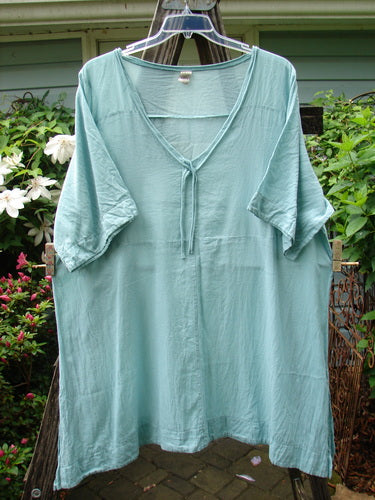 Barclay Batiste Deep Neck Tie Dress Unpainted Spearmint Size 2, short-sleeved, displayed hanging on a clothesline. The fabric appears lightweight and suitable for casual, creative expression.