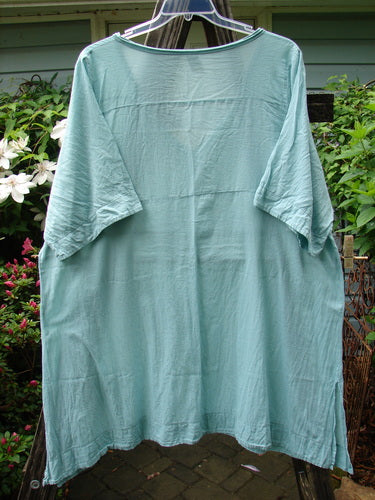 Barclay Batiste Deep Neck Tie Dress Unpainted Spearmint Size 2 hangs on a clothesline, showcasing its short sleeves and elegant cut.