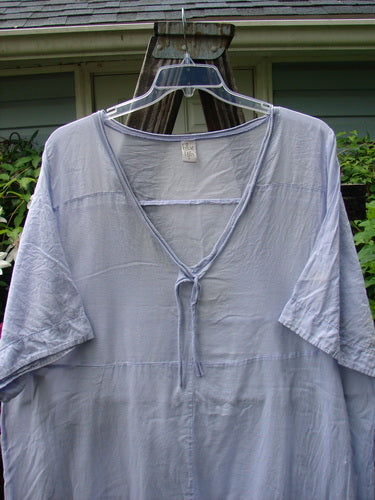 Barclay Batiste Deep Neck Tie Dress Unpainted Lilac Size 2 displayed on a hanger, showcasing its short sleeves and slight light blemish on the lower sleeve.