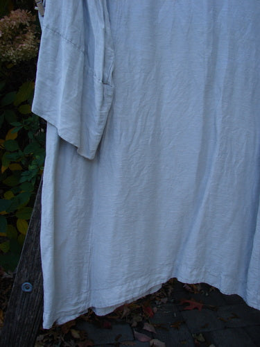 Barclay Hemp Silk Single Button Cardigan Unpainted Dew Size 2 draped over a wooden support, showcasing its deep V neckline, wide banded sleeves, and curved vertical seams, displayed outdoors.