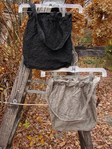 2000 NWT Shaunting Silk Bags Unpainted Black and Cement OSFA are displayed on hangers outdoors, showcasing their crinkle silk texture, elastic-topped closure, and medium shoulder strap among natural surroundings.