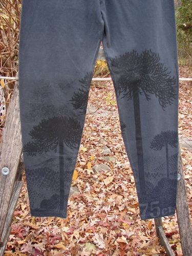 Barclay Cotton Lycra Straight Pant Shadow Tree Lux Silhouette Size 1: Dark gray full-length leggings with forest-themed print on lower legs, displayed outdoors over a wooden ladder amid a fall setting.