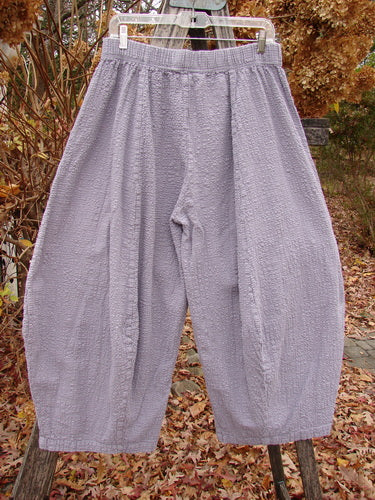 Barclay Pucker Crop Mojo Pant Unpainted Lavender Size 1, featuring a unique 3D diamond cut, elastic waistband, wide legs, and exterior flop front pockets, displayed hanging outdoors against a leafy backdrop.