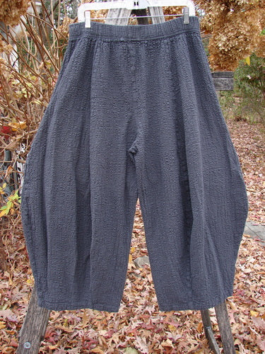 Barclay Pucker Crop Mojo Pant Unpainted Ironworks Size 1, showcased outdoors, features a textured, dark-gray, cropped design with 3D diamond-shaped drape from the knee and generous front pockets.