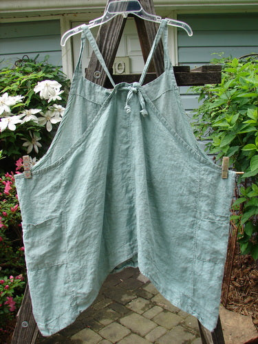 Vintage Barclay Linen Drop Pocket Apron in Seafoam hanging outdoors on a clothesline. Features adjustable straps, drop sides, and double front pockets. Unpainted for easy layering. Perfect for creative expression.