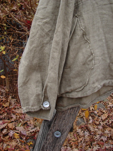 Magnolia Pearl Linen Crop Artist's Pocket Pullover Light Army OSFA draped on a post, showcasing its billowy three-quarter sleeves with pearl cuff buttons and varying hemline, highlighting its artisanal design.
