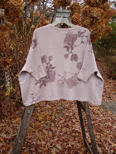 Barclay Colors Sweatshirt Dogwood Branch Pink Blush OSFA draped on a wooden ladder, featuring a dark floral pattern on mid-weight organic cotton fleece with dolman banded sleeves and contrasting side panels.