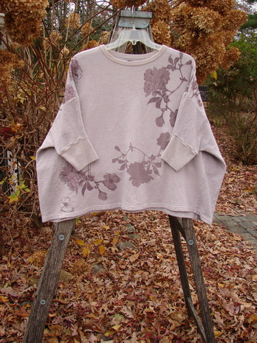 Barclay Colors Sweatshirt Dogwood Branch Pink Blush OSFA features a floral motif on a light-lavender pullover, displayed on a ladder amidst an autumn garden, reflecting Bluefishfinder.com's unique vintage-inspired style.