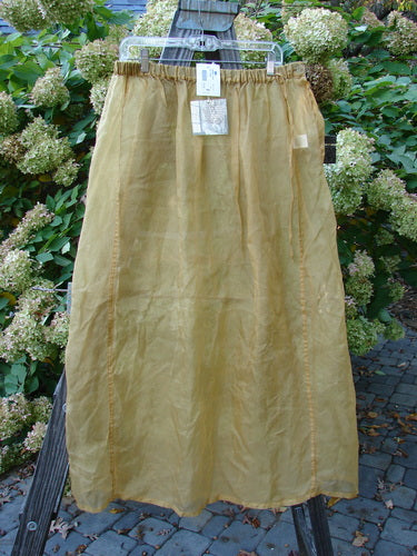 2000 NWT Silk Organza Skirt Unpainted Bone Size 2: A skirt on a tree, featuring a long yellow skirt with a white tag. The skirt has a lovely sheer bone hue and displays grace with movement.