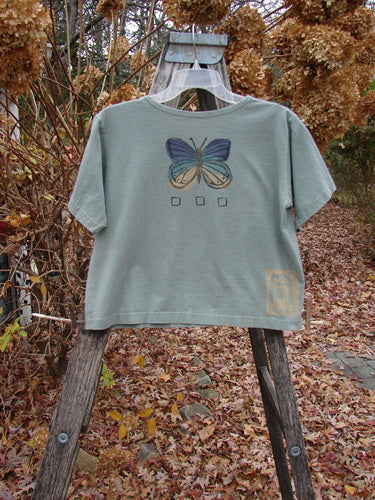 1996 Crop Tee Floral Butterfly Cricket Size 1 displayed on a rustic wooden step-ladder outdoors, showcasing a stylized butterfly graphic and three small square outlines, embodying Bluefishfinder.com's vintage, expressive style.