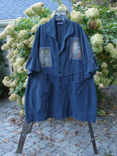 A Barclay PMU Patched Twill Decora Brushed Flutter Coat in Navy, featuring a larger fold-up neckline, dark matching buttons, a wrap-around waistline, flutter ruffle sleeves, giant round bottom pockets, and a swingy hemline. Fully patched in a falling leaf theme. Size 2.