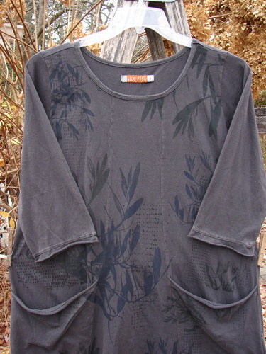 Barclay Sunny Day Pocket Tunic Dress Flutter Bamboo Steel Meteorite Size 1, featuring a tone-on-tone leaf print, three-quarter sleeves, rounded neckline, and two front pockets, displayed on a clear hanger outdoors.