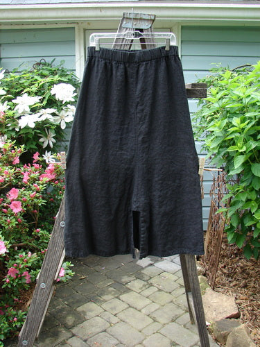 A black Barclay Linen Double Button Back Vent Skirt, size 2, displayed on a wooden ladder, highlighting its full elastic waistline and unique front double button vents.