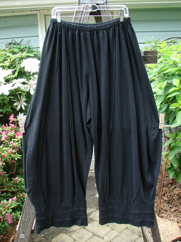 A pair of Barclay Reverse Stitch Contrast Cuff Pant Unpainted Black Size 2, featuring full elastic waistline, rippled cuffs, and sectional panels, displayed on a wooden board.
