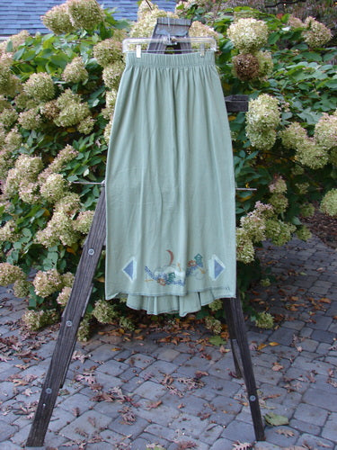 1995 Kick Pleat Skirt, Spanish Moss, Size 1: A skirt on a rack with a widening shape, sassy rear kick pleat, and painted accents on the waistband.